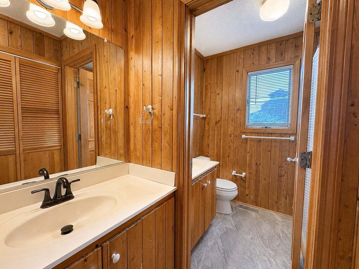 Une salle de bain aux murs lambrissés, équipée d’un lavabo, d’un miroir et de toilettes.