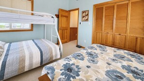 Une chambre avec des lits superposés, une armoire en bois et une fenêtre avec des stores.
