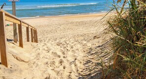 A sandy beach with wooden steps leading down to the water, surrounded by grass.