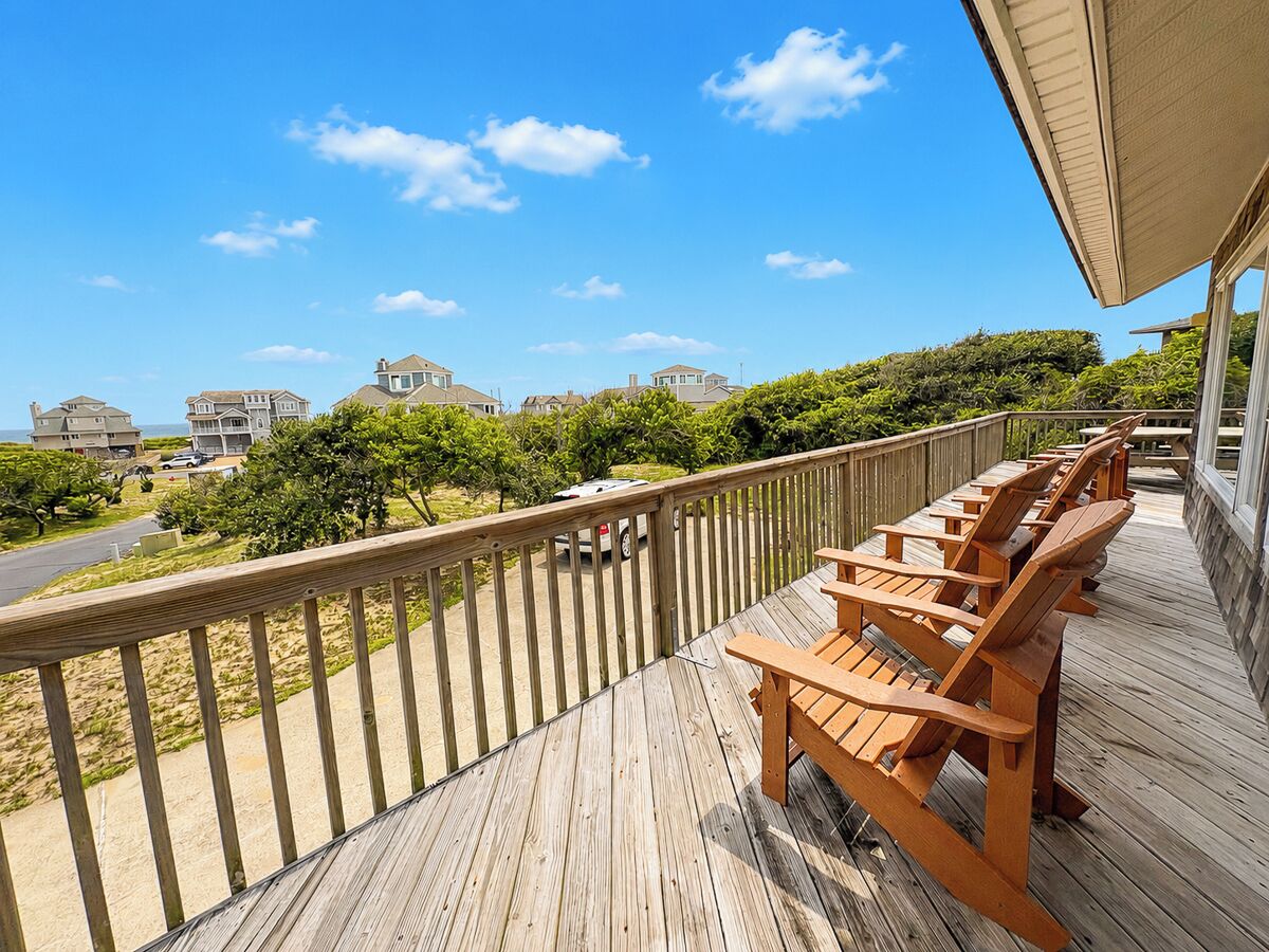 Eine Holzterrasse mit Sitzgelegenheit und Blick auf Häuser und Grünflächen.