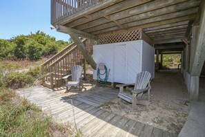 A wooden deck with two Adirondack chairs, a white storage unit, and a staircase leading to a covered area.