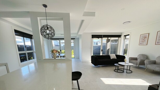 A spacious living area with a black sofa, a round coffee table, and a grey armchair. A large window provides a view of the outside.
