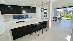 A modern kitchen with a large island, black cabinets, and a dining area with a table and chairs.