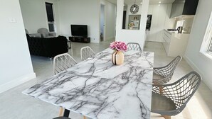 A modern dining area with a marble table, wire mesh chairs, and a vase of flowers.