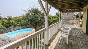 Eine Holzterrasse mit Pool, weißen Stühlen und einem überdachten Bereich.