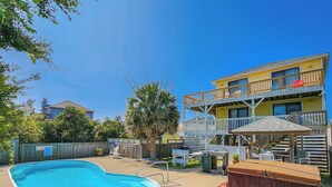 Ein Garten mit Swimmingpool, einer Holzterrasse, Gartenmöbeln und einem zweistöckigen Gebäude mit Balkon.