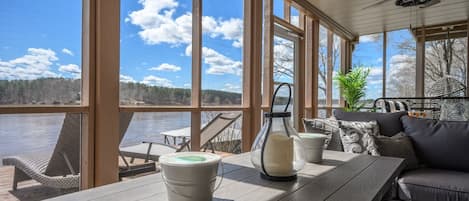 A covered deck with a view of a lake, wooden furniture, and a ceiling fan.