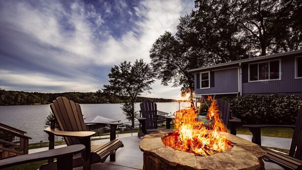 Un foyer entouré de fauteuils Adirondack, une terrasse et une vue sur un lac et une maison.