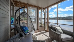 Une véranda aménagée avec des meubles en osier, un fauteuil suspendu et une vue sur un lac.