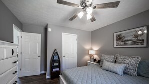 Une chambre à coucher comprenant un lit, une commode, une table de chevet, une lampe et un ventilateur de plafond.