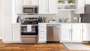 Una cocina moderna con armarios blancos, electrodomésticos de acero inoxidable, una barra de café y lavavajillas.