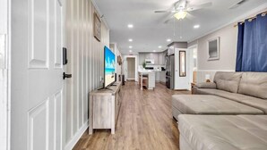 A modern living room with a sofa, a TV, and a dining area. - Amazing Home on Main St - Walk to the Beach (North Myrtle Beach)