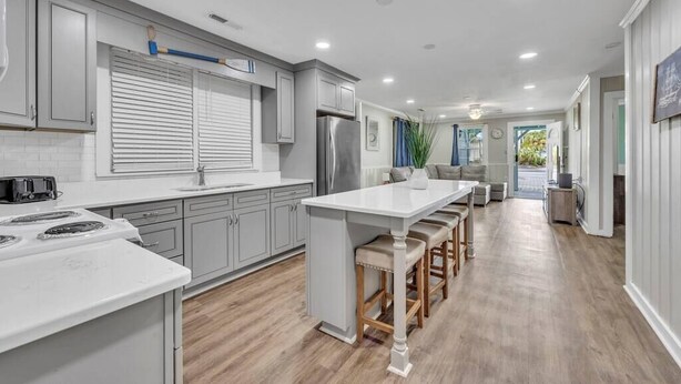 A modern kitchen with grey cabinets, a central island with stools, a built-in oven, and a refrigerator. - Amazing Home on Main St - Walk to the Beach (North Myrtle Beach)