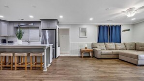 A modern kitchen with grey cabinets, a stainless steel refrigerator, and wooden stools. - Amazing Home on Main St - Walk to the Beach (North Myrtle Beach)