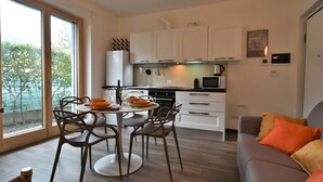 A modern kitchen with white cabinets, a dining table with chairs, and a view of greenery outside. - Olmo Garden Apartment by Interhome (Valtellina)