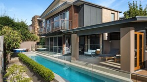 Une maison moderne dotée d’une piscine, d’un espace salon extérieur et d’un patio couvert.