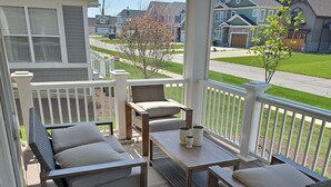 A covered outdoor seating area with a table and chairs, a rug, and a large planter.