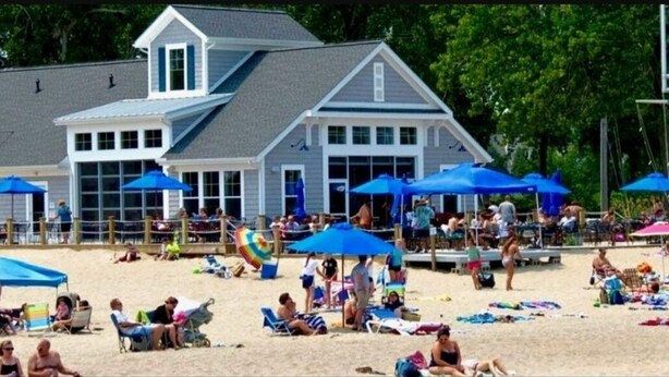A beachside building with multiple blue umbrellas, beach chairs, and people relaxing.