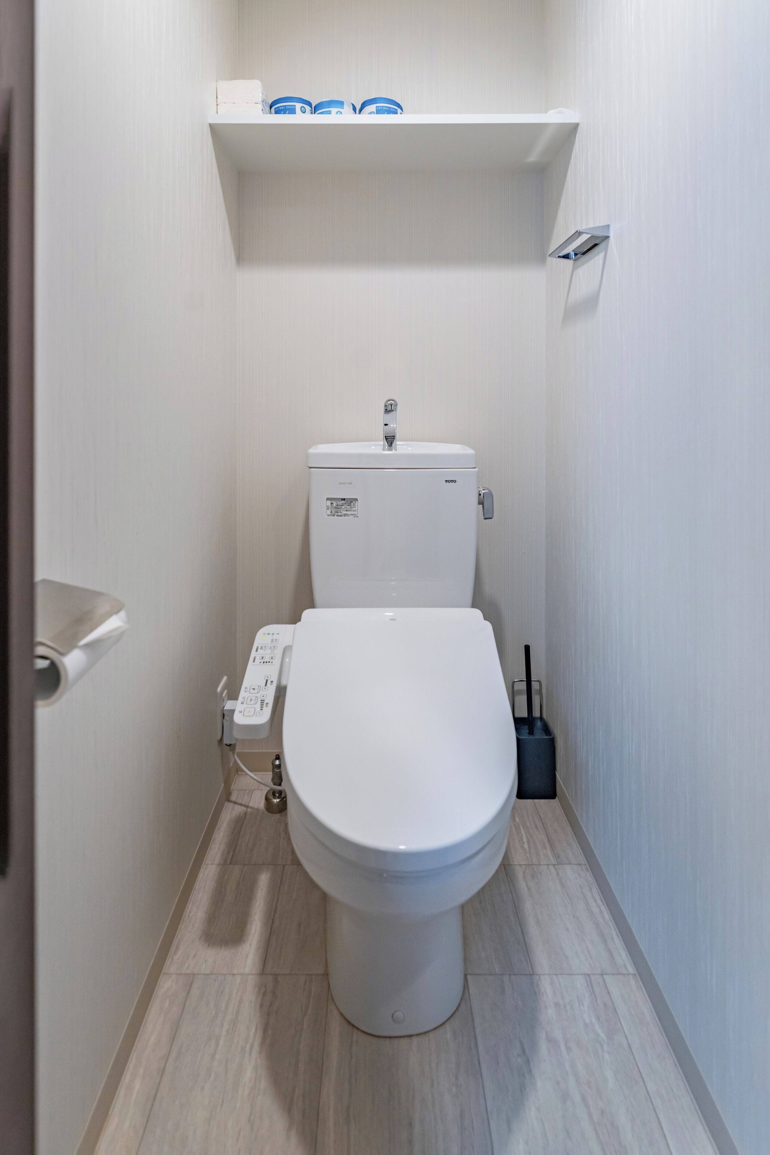 A small, modern bathroom with a toilet, a shelf above the toilet, and a hand dryer.