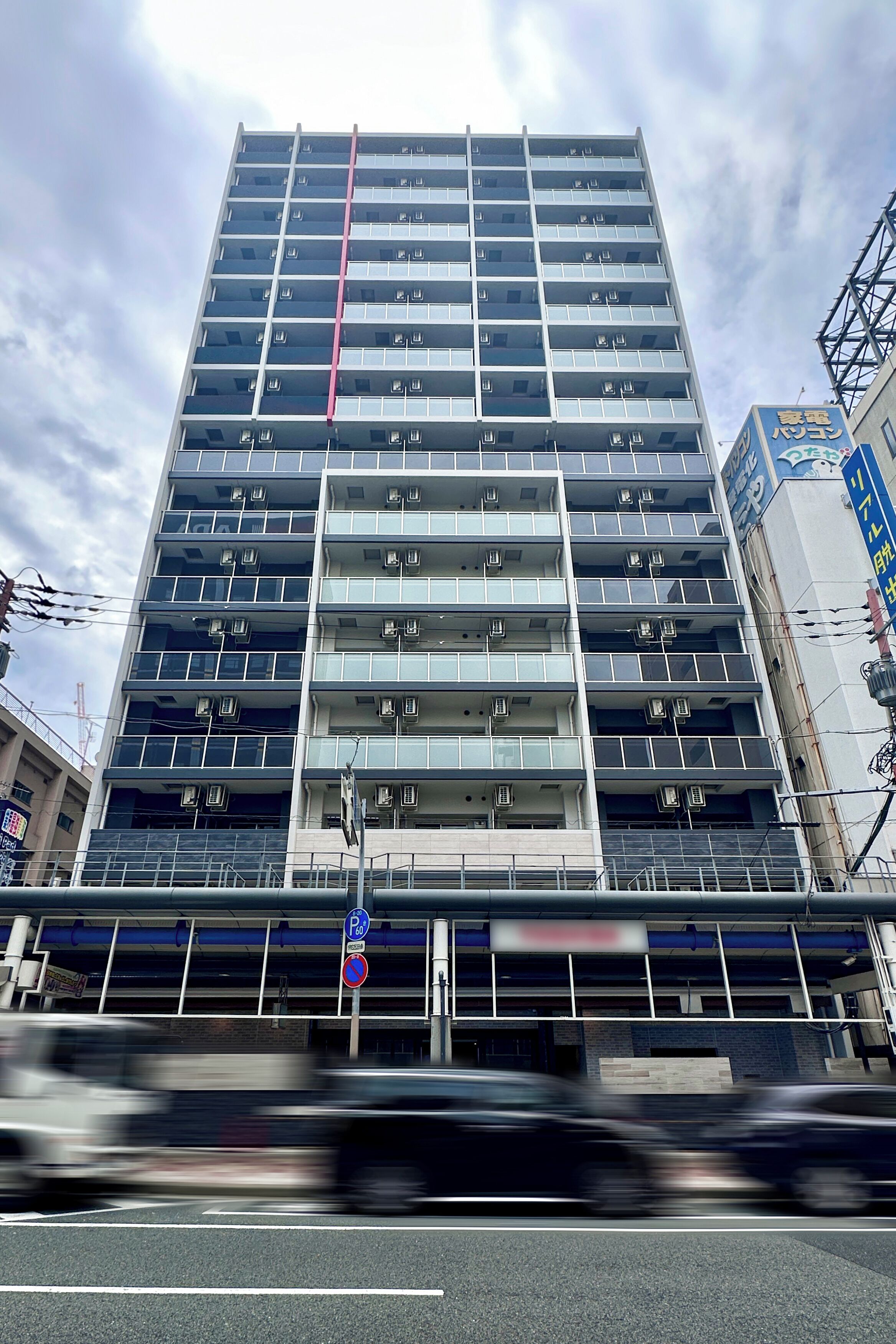 A multi-story building with a central vertical feature, a parking garage below, and a sign indicating a parking area.