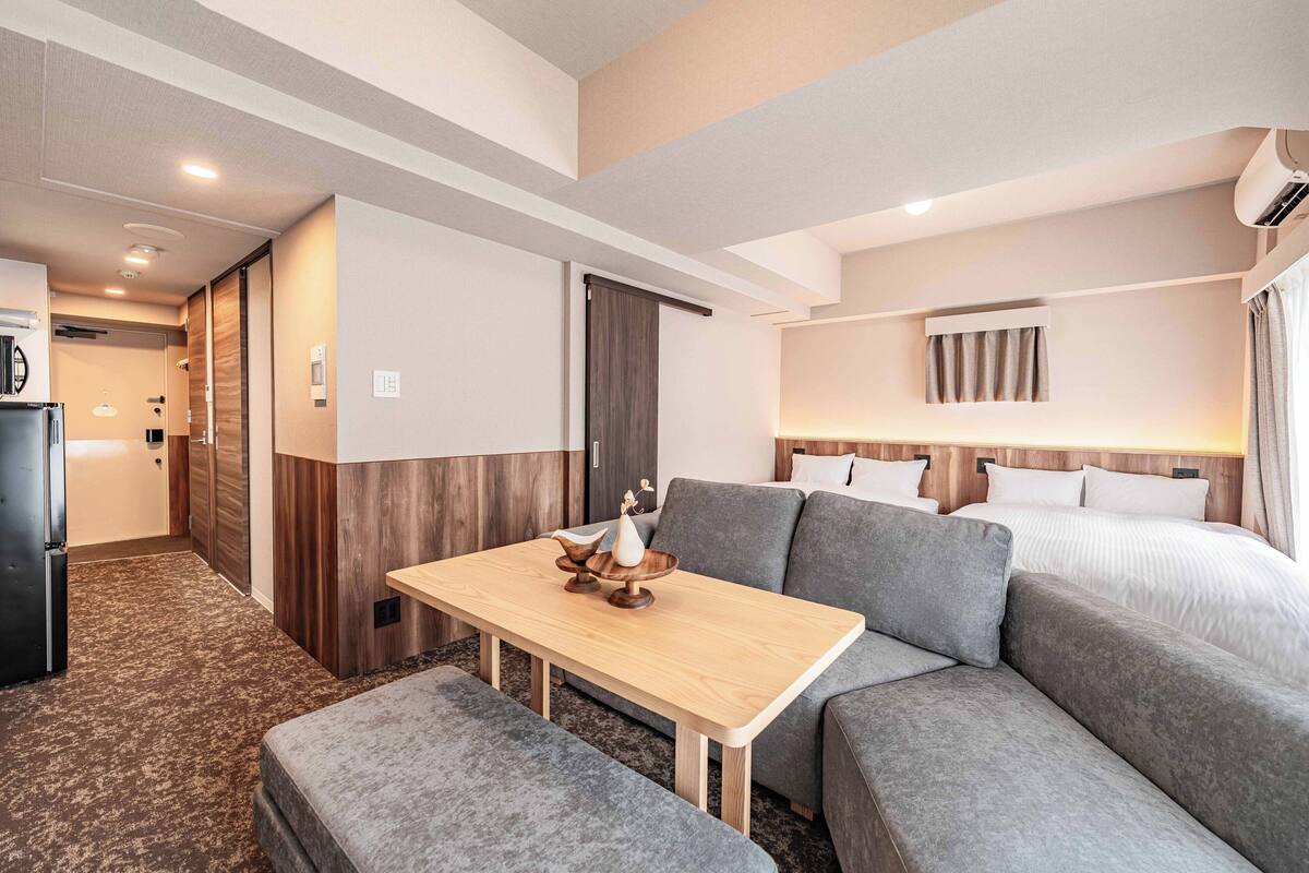Una habitación de hotel moderna con sofá, una mesa de comedor, una cama y una kitchenette.
