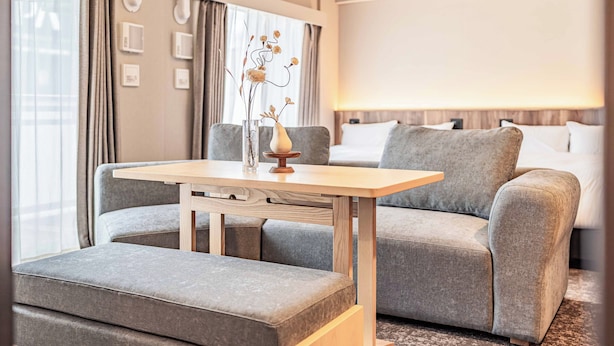 A hotel room with a grey sofa, a wooden table, a vase with flowers, and a bed with white bedding.
