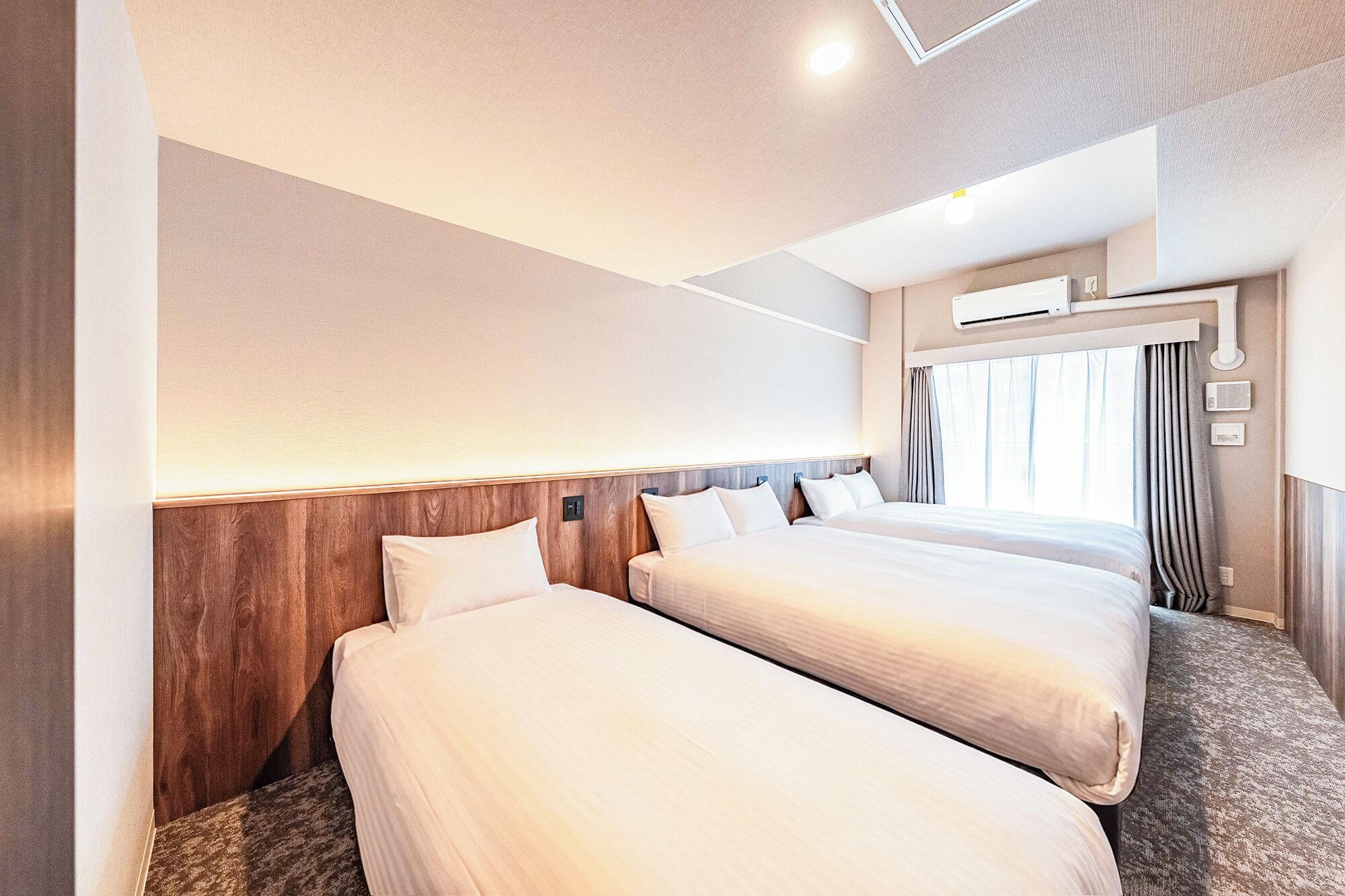 A hotel room with two beds, a wooden headboard, a ceiling light, and a window with curtains.
