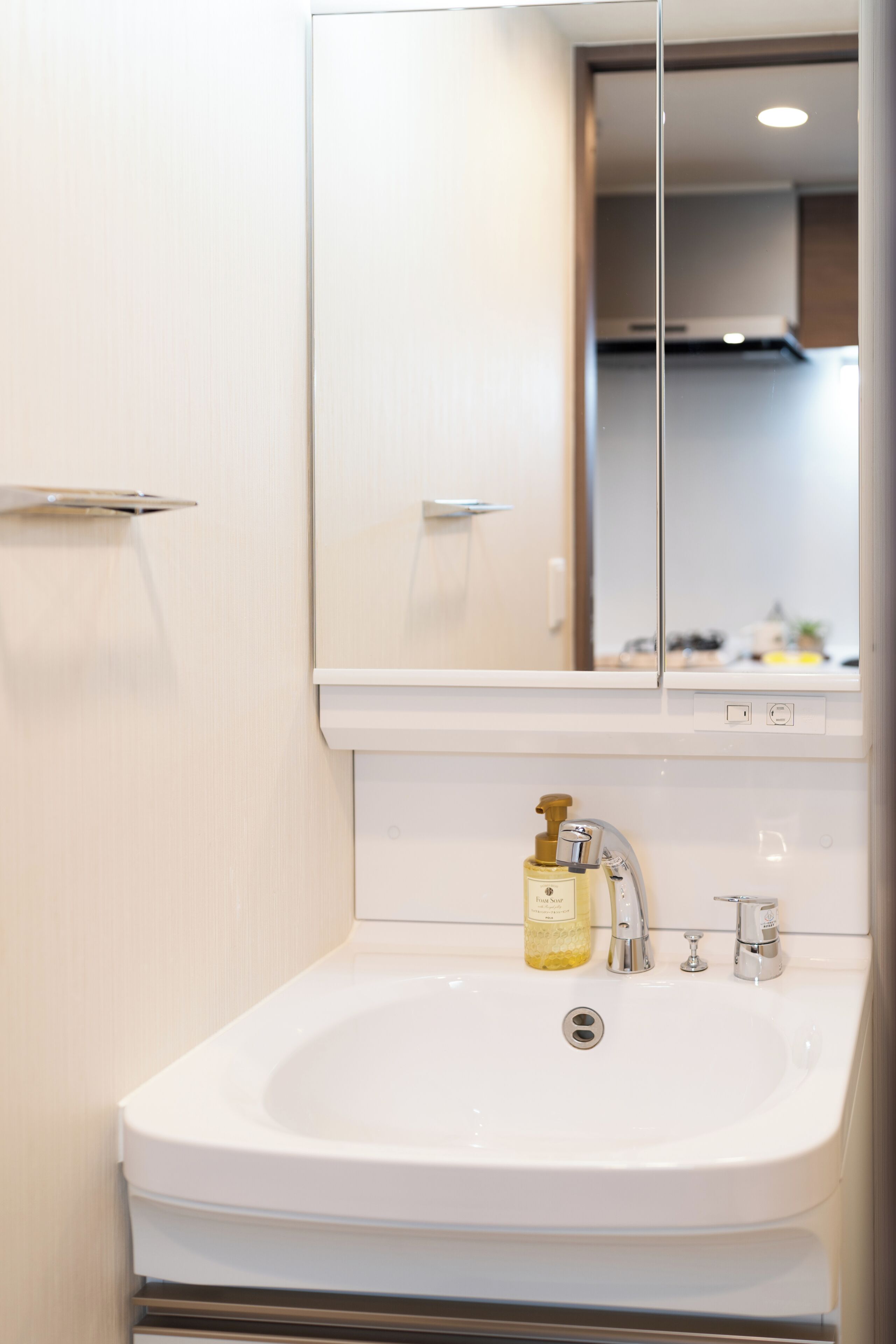 A white bathroom sink with a mirror above it, a soap dispenser, and a faucet.