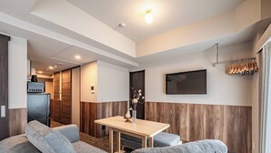 A modern hotel room with a sofa, a small table, a TV mounted on the wall, and a coat rack.