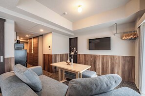 A modern hotel room with a sofa, a small table, a TV mounted on the wall, and a coat rack. - Apartment Hotel 11 Namba-Minami Ebisucho (Osaka)