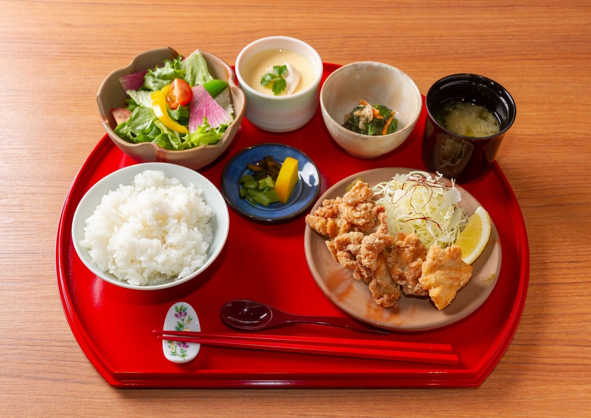 A tray with various Japanese dishes including rice, fried chicken, and a salad.