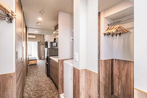 A narrow hallway with wooden paneling, a white refrigerator, a coffee maker, and a hanging clothes rack. - Apartment Hotel 11 Namba-Minami Ebisucho (Osaka)