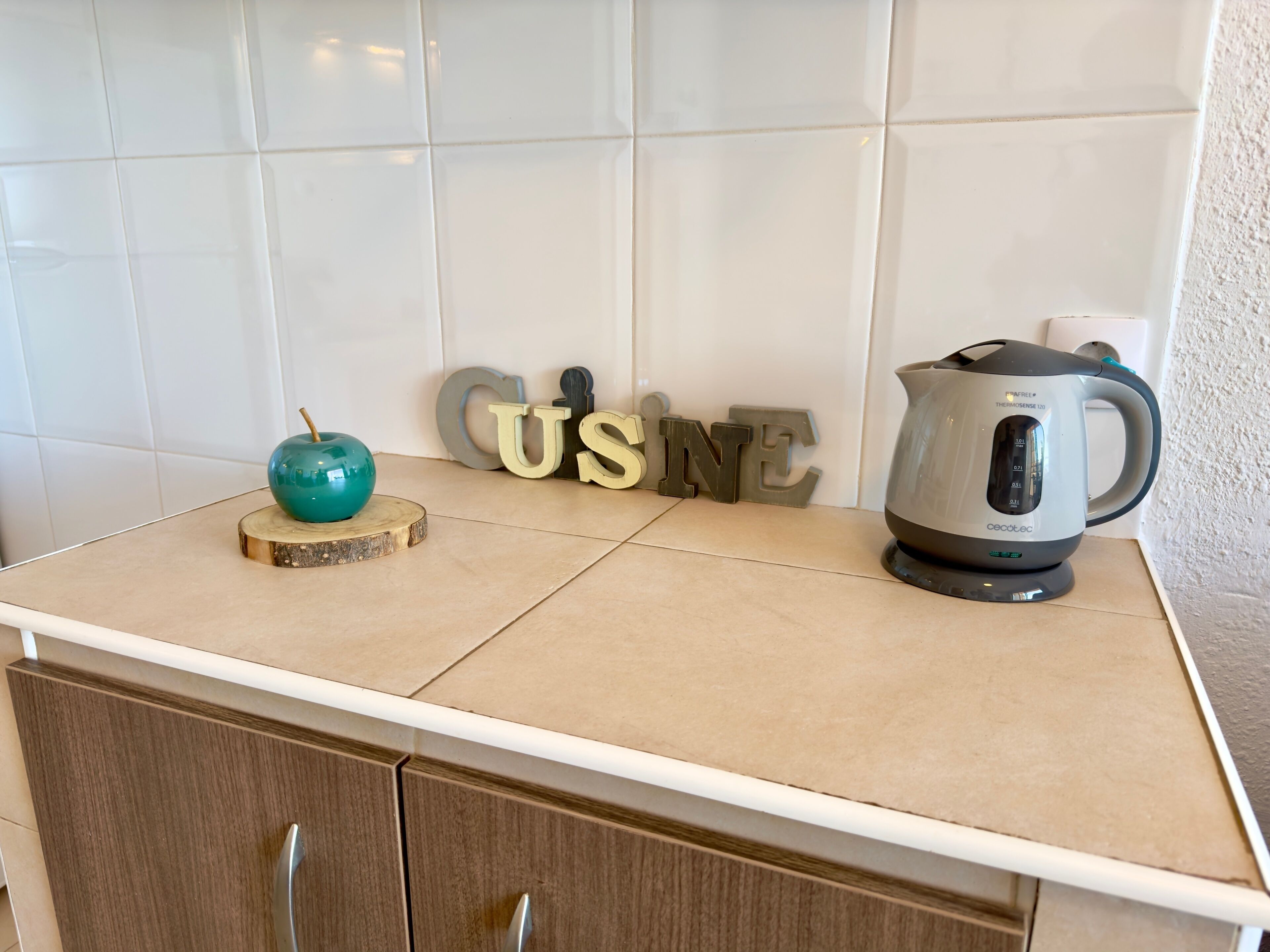 A kitchen counter with a teal apple on a wooden coaster, a coffee maker, and decorative letters spelling "GO HOME".