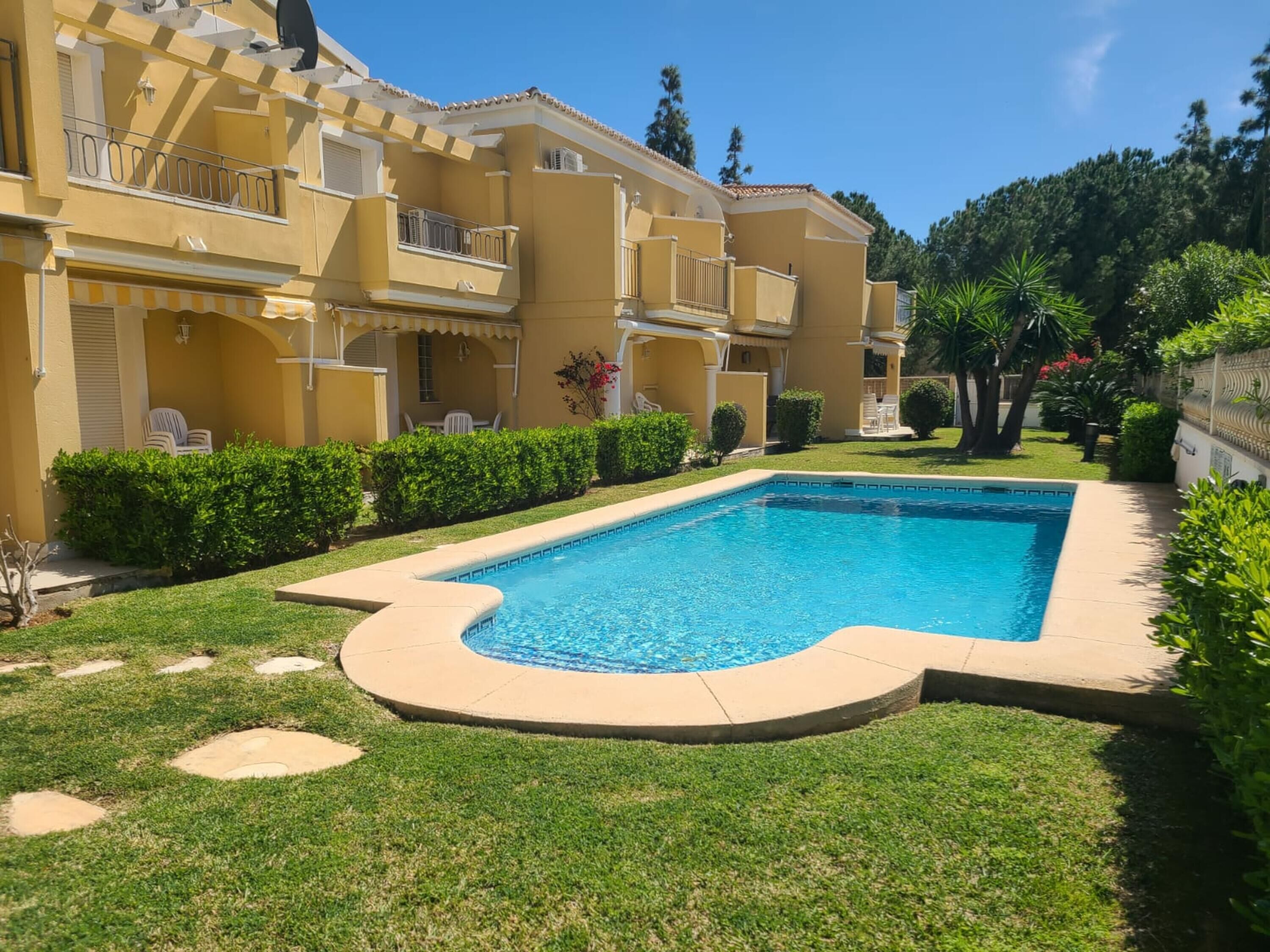 Una piscina envoltada per un jardí ben cuidat i setges, amb un edifici de diversos pisos al fons.