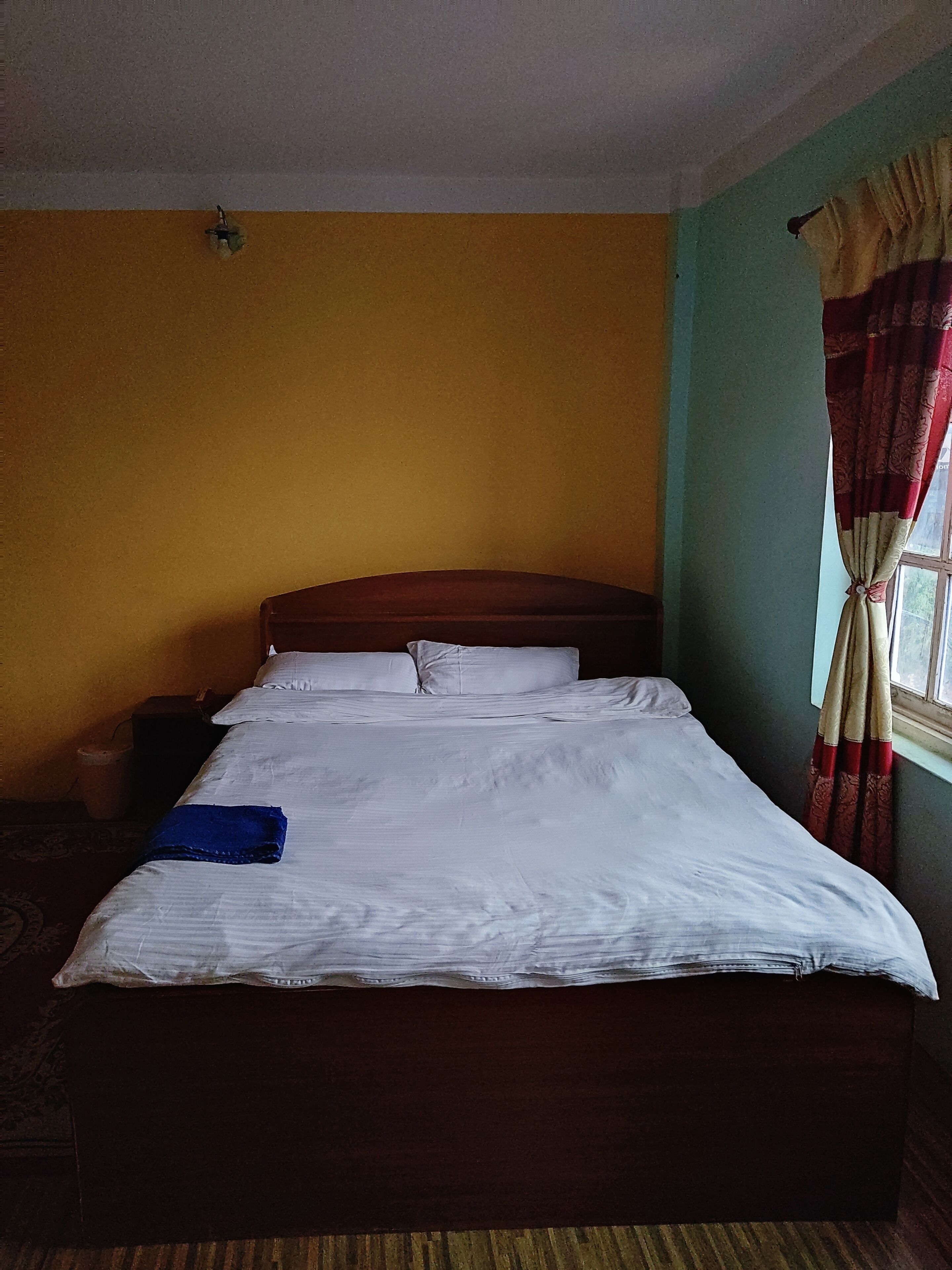 A single bed with white linens, a wooden headboard, and a blue towel on the bed.