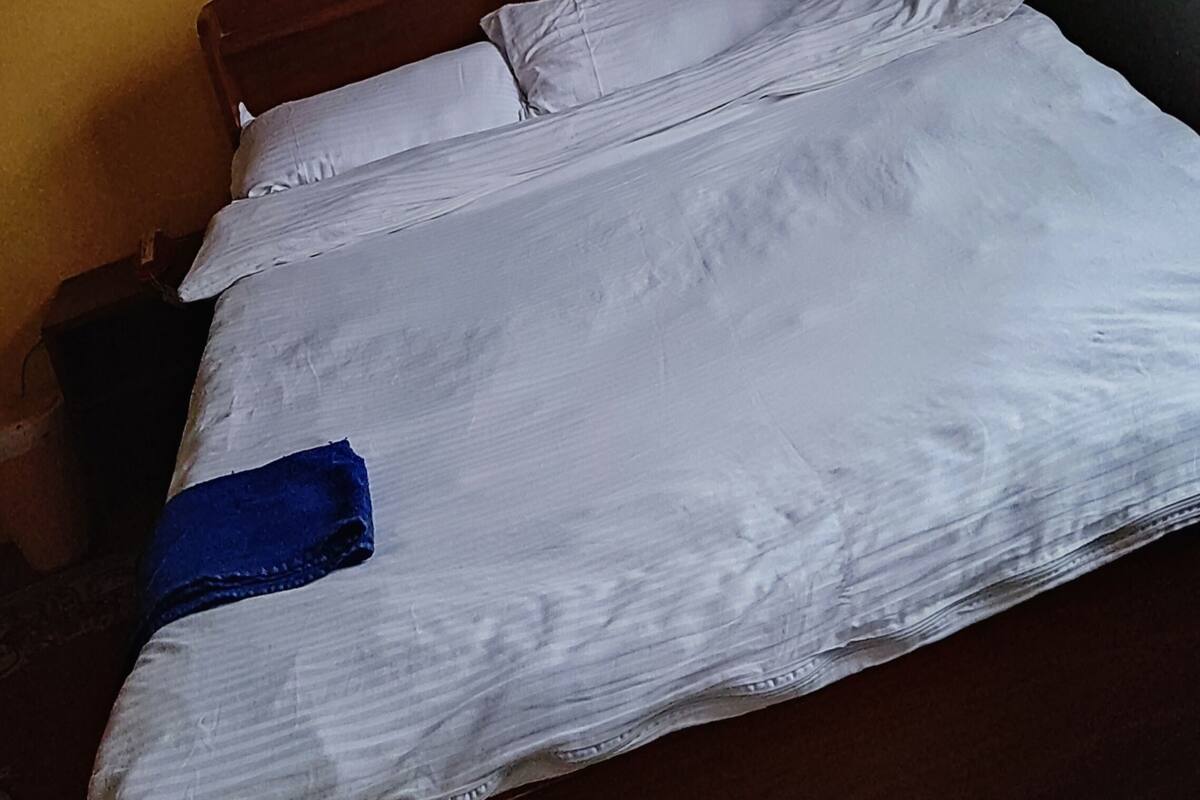 Una cama con ropa de cama blanca y una toalla azul, cabecera de madera y mesita de noche con lámpara.
