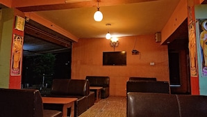 L’intérieur d’un restaurant est aménagé avec des tables et des chaises en bois, un luminaire suspendu et un téléviseur fixé au mur.