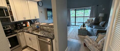 A modern kitchen with stainless steel appliances, a granite countertop, and a dining area with a view of the outdoors.