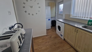 A compact kitchen with a built-in washing machine, a toaster, and a clock on the wall. - House - Sleeps 4 - Garden - Parking (Wallsend)