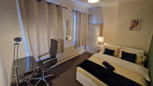 A hotel room with a bed, a desk with a chair, a lamp, and a mirror. - House - Sleeps 4 - Garden - Parking (Wallsend)