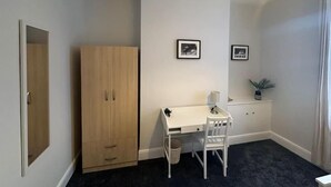 Una habitación pequeña con un escritorio blanco, una silla blanca, un armario de madera y dos cuadros en la pared.