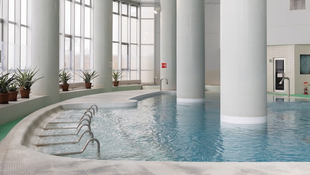 An indoor swimming pool with clear water, surrounded by large windows and white pillars. - Tabist Heilsam Kurikoma Cottage (Kurihara)