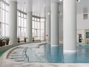 An indoor swimming pool with clear water, surrounded by large windows and white pillars. - Tabist Heilsam Kurikoma Cottage (Kurihara)