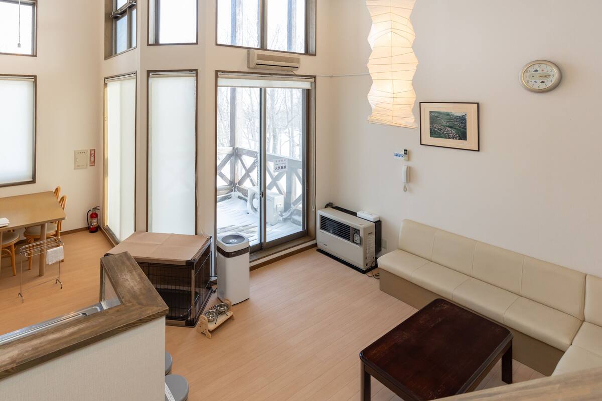 A spacious living room with a wooden floor, a sofa, a coffee table, and a dining area with a table and chairs.