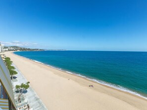 A beach with a clear view of the ocean and a building with balconies overlooking the beach.