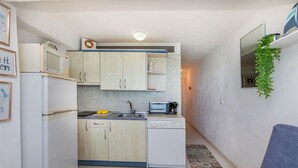 Une cuisine compacte équipée d’un four à micro-ondes, d’un grille-pain, d’un évier et d’un petit réfrigérateur. Le salon comprend un canapé bleu et une plante.