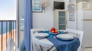 Un balcon avec une table dressée pour deux personnes, un ventilateur, une télévision et un réfrigérateur.