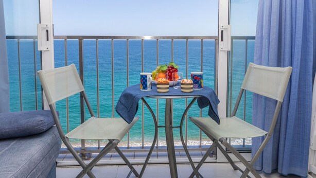 Un balcon avec une table dressée pour deux personnes, donnant sur une mer turquoise.