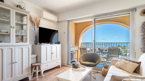 Un salon moderne doté d’un téléviseur, de meubles blancs, d’un coin repas et d’un balcon offrant une vue sur la mer.