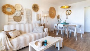 Un salon avec un canapé à rayures, une table basse sur laquelle est posée une bougie, et un coin repas avec des chaises blanches et une table en bois.